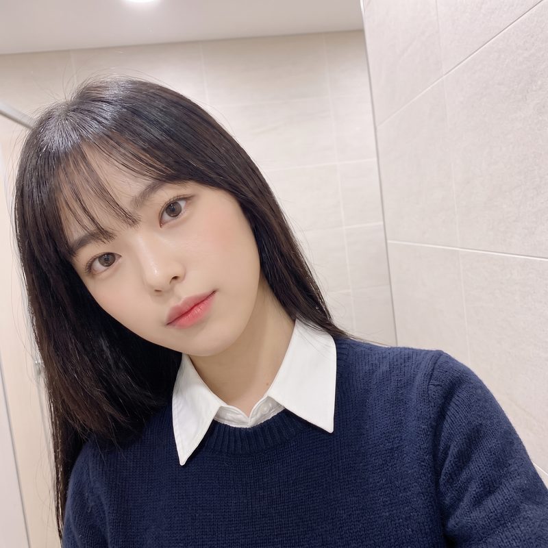 밝은 타일 벽 앞에서 니트를 입은 여성 방문객의 데일리 셀피 예시 이미지