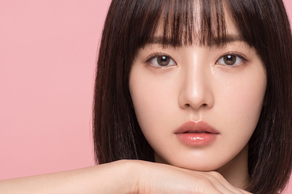 파스텔 핑크 배경에서 손등에 턱을 괸 여성 모델의 뷰티 클로즈업 (AI 생성 예시 이미지)
