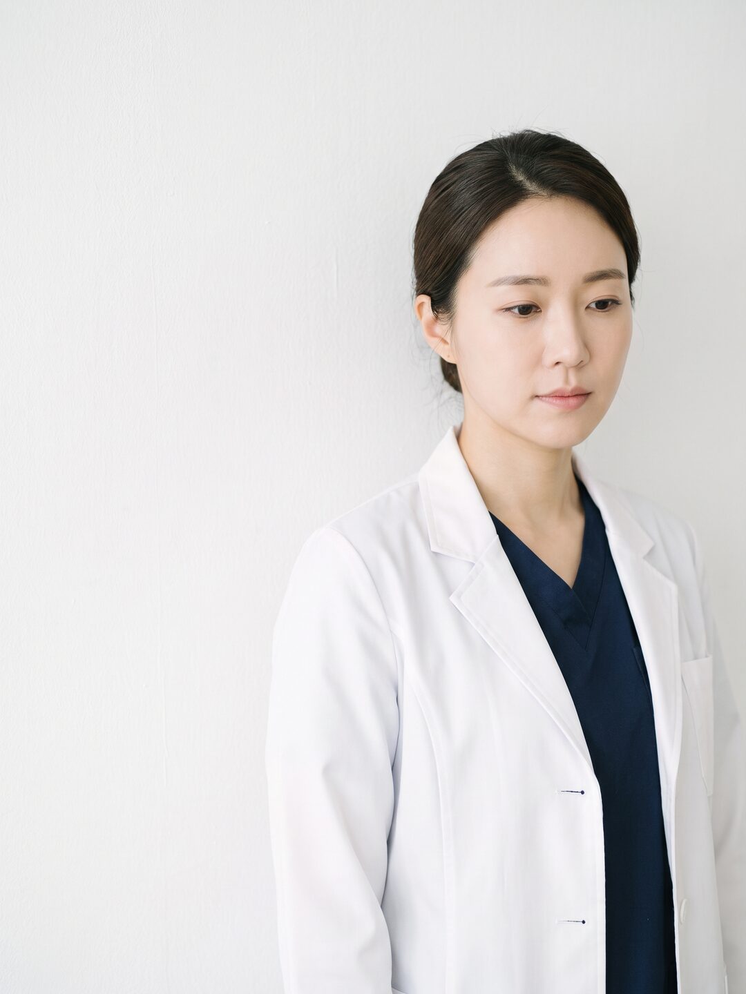 흰 가운을 입은 리뷰티 진료원장이 밝은 벽 앞에 서 있는 모습