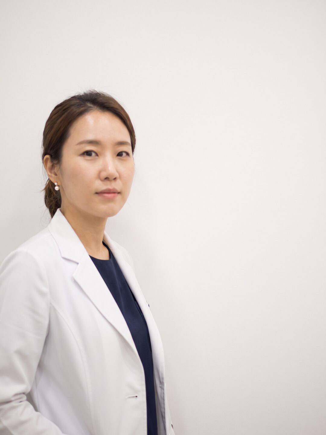 밝은 흰 벽 앞에서 차분한 표정으로 서 있는 리뷰티 의료진 (AI 생성 예시 이미지)