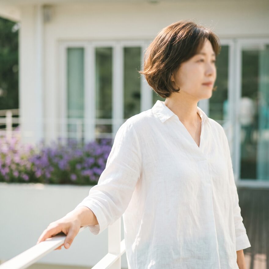 실외 난간 곁에 서서 편안하게 미소 짓는 리뷰티 안면 웰니스 담당 원장 (AI 생성 예시 이미지)