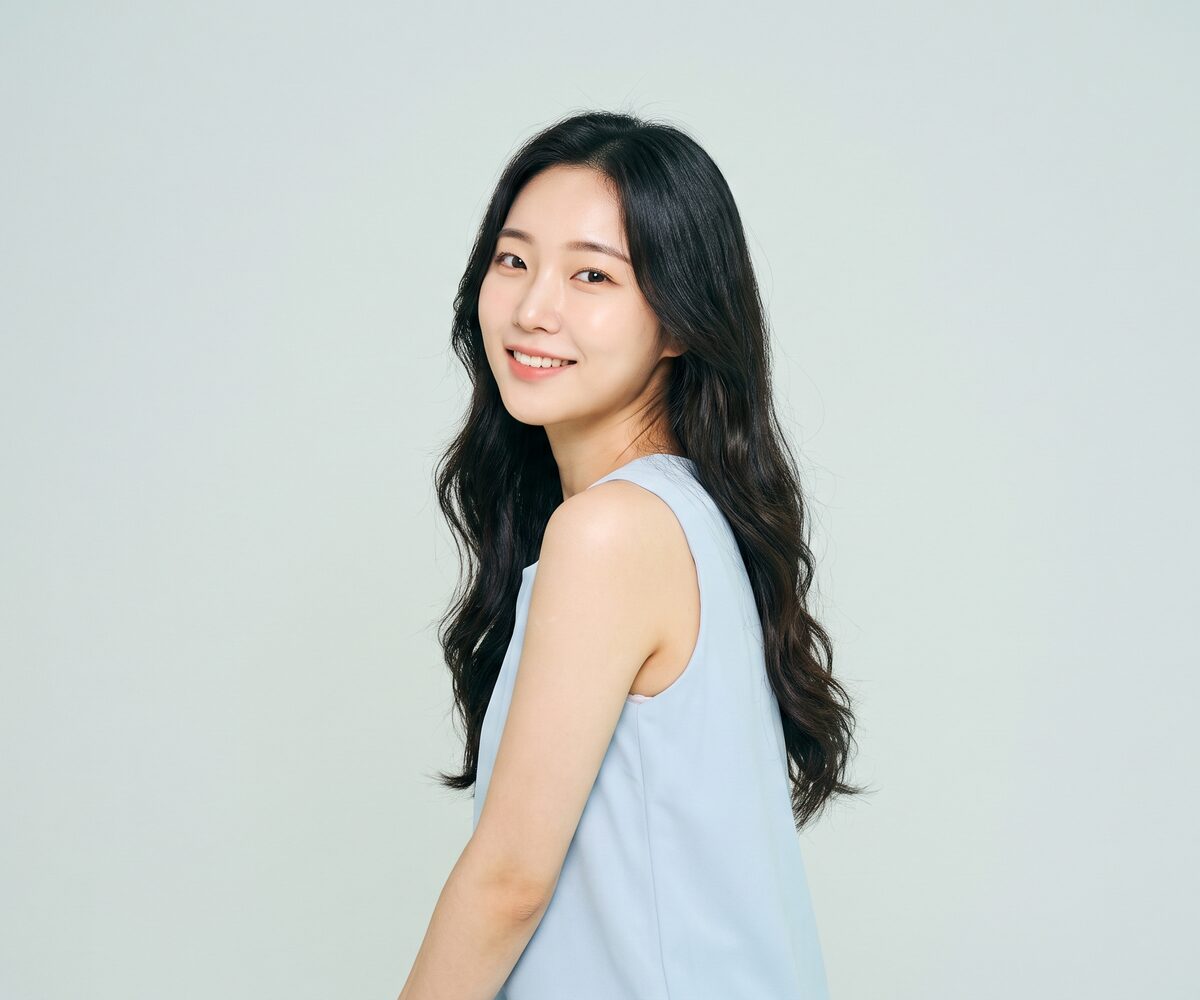 연한 하늘색 톱을 입은 여성이 편안하게 서서 웃는 체형 웰에이징 이미지 (AI 생성 예시)