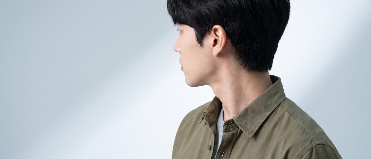 밝은 그레이 스튜디오 배경 앞에서 정면을 바라보는 20대 남성 모델의 상반신 배너 컷 (AI 생성 예시 이미지)