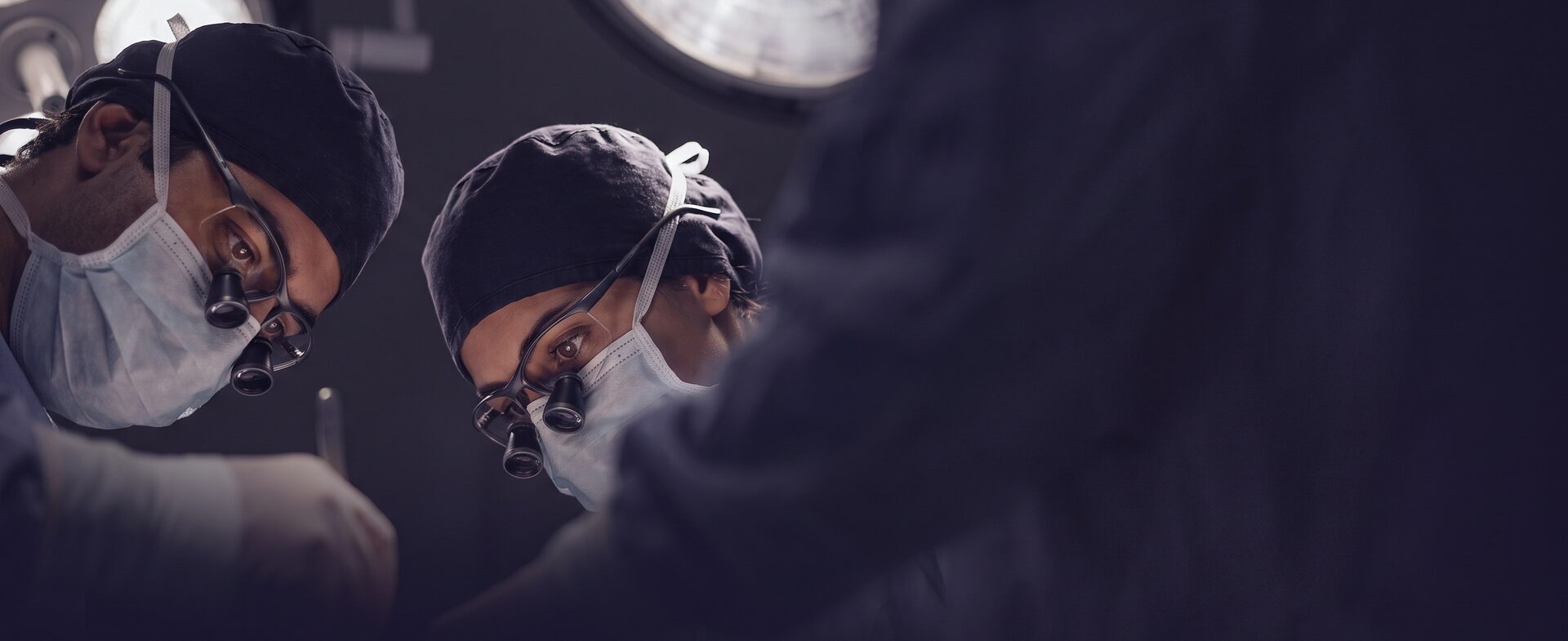 수술등 아래 마스크와 캡을 착용한 익명 의료진이 시술실에서 집중하는 분위기 컷