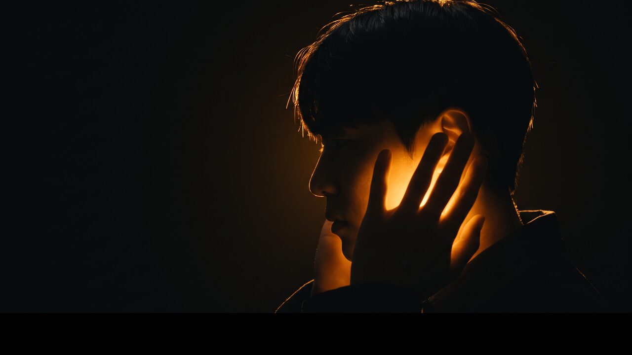 턱과 귀 주변을 손으로 감싼 인물의 측면 실루엣과 은은한 광원 효과